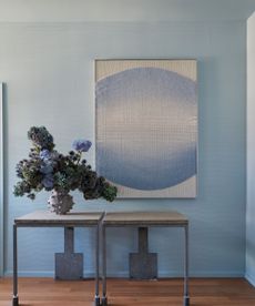 light blue wall with light blue artwork, gray metal table, vase of flowers, wooden floor