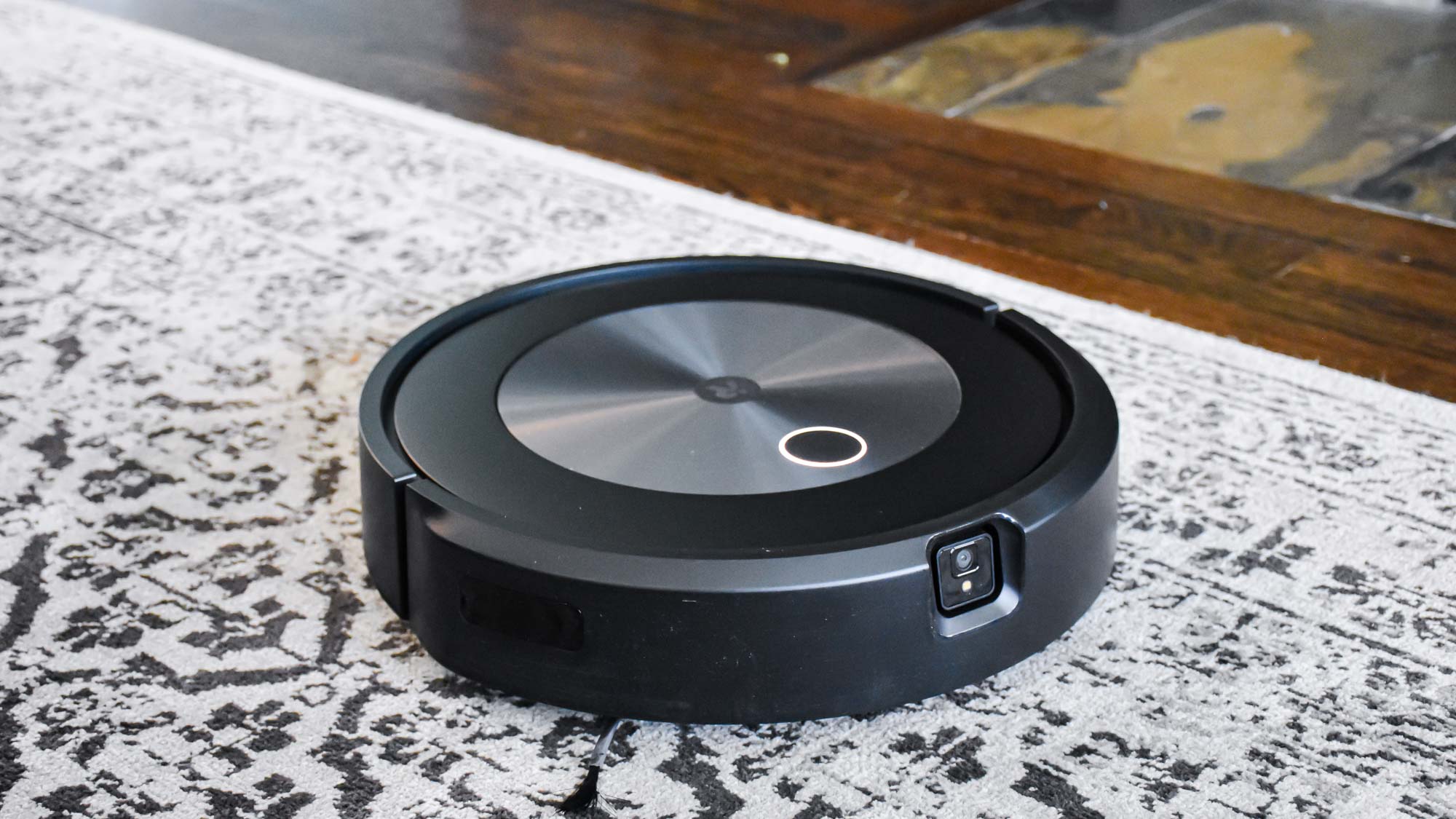 A iRobot Roomba j7+ on a black and white carpet on top of hardwood