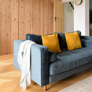 A living room with a blue velvet sofa, parquet flooring and slat wall panelling