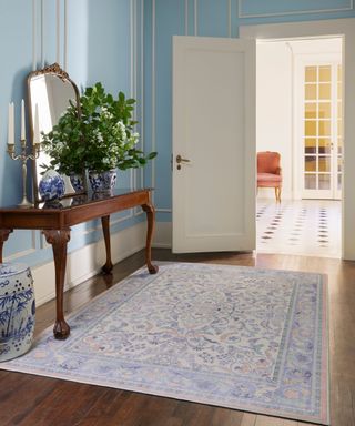 An entryway area with light blue and white paneled walls, a dark brown wooden vanity, blue and white vases, and a purple and pink patterned rug on a dark brown wooden floor