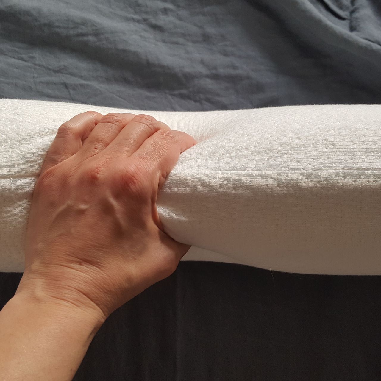 The Panda Memory Foam pillow is on its side and squeezed by a hand.