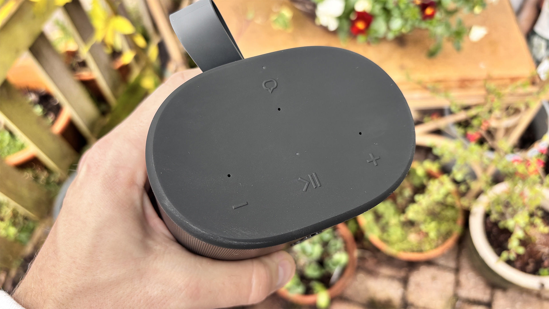 Sonos Play wireless speaker held in hand above garden patio showing top of speaker and controls