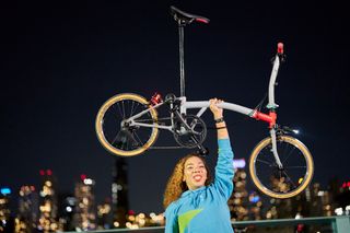 Image shows cyclist holding aloft a Brompton CHPT3 v4 folding bike in New York City