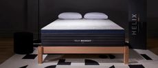 Helix Midnight Luxe mattress review image shows the hybrid bed on a wooden bed frame on a black and white rug