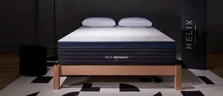 Helix Midnight Luxe mattress seen on a wooden bed frame on a black and white rug