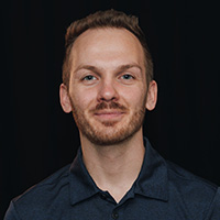 Headshot of Alex Panasyuk wearing dark blue shirt against black background.