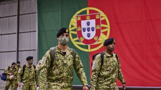 Portuguese soldiers marching in front of the nation's flag inside a hangar