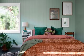 Bedroom with soft green panelled walls, terracotta bedding and black framed pictures