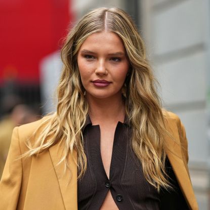 woman with blonde wavy hair wearing a brown cardigan and blazer