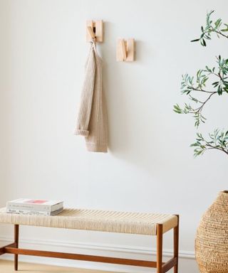 An entryway with a gray cardigan on a wooden hook, with a plant next to it and a bench underneath it