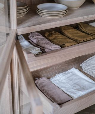 cabinet with pullout drawers holding different colored napkins and earthenware plates on a shelf above