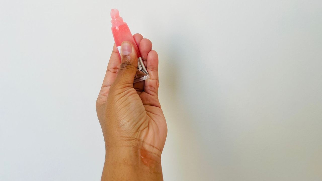 A person holding an opened Neutrogena SPF Lip balm with a gloss-like consistency.