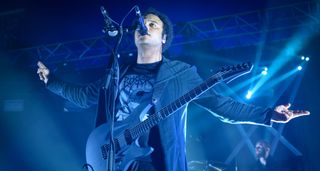 Manuel Gagneux of Zeal & Ardor performs onstage with his Aristides S-style bathed in blue light