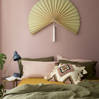 blush pink and green bedroom with fan on wall above bed, navy and brass desk lamp, folk textured cushion, green and blush bedding, turmeric coloured sheet, plant