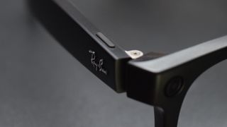 Close-up photograph of Ray-Ban Meta smart glasses hinge, Ray-Ban branding, and button.