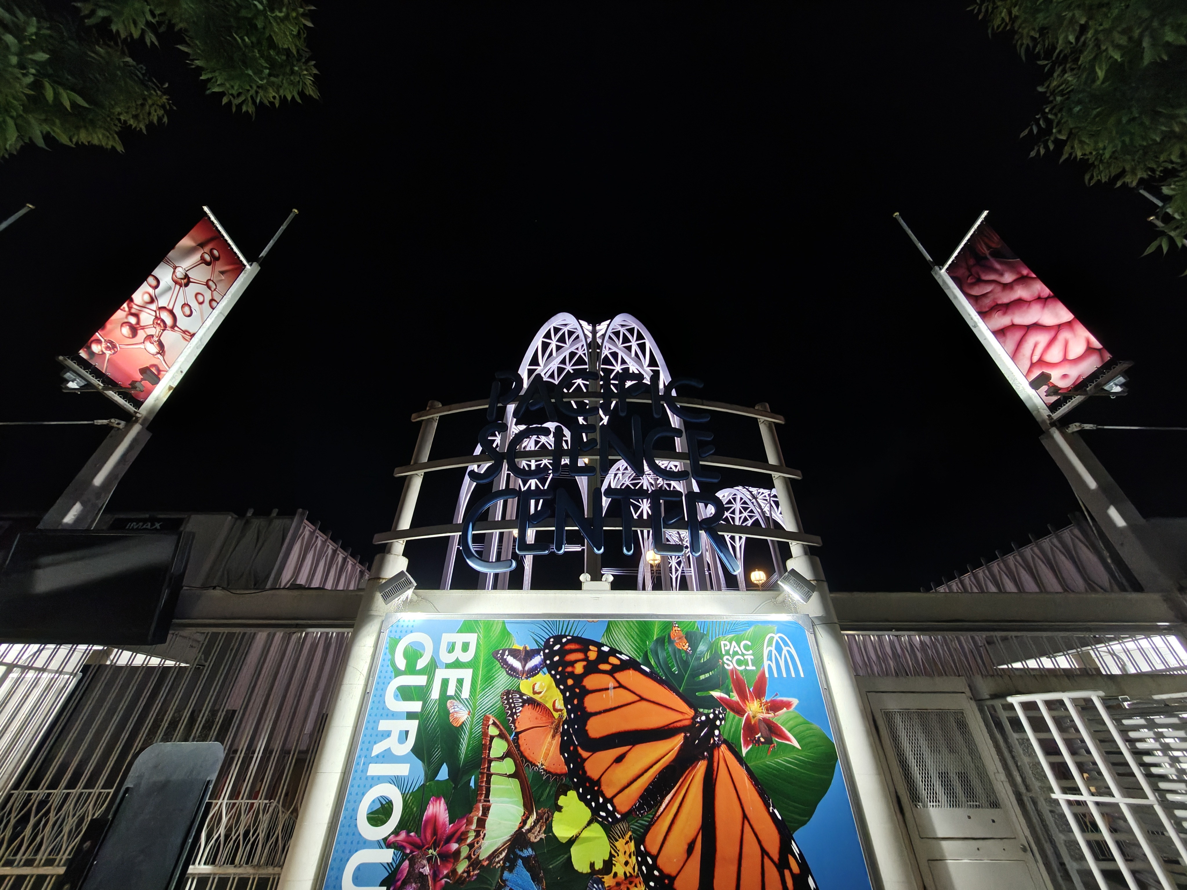 A gated entrance lit up at night with a butterfly poster in front