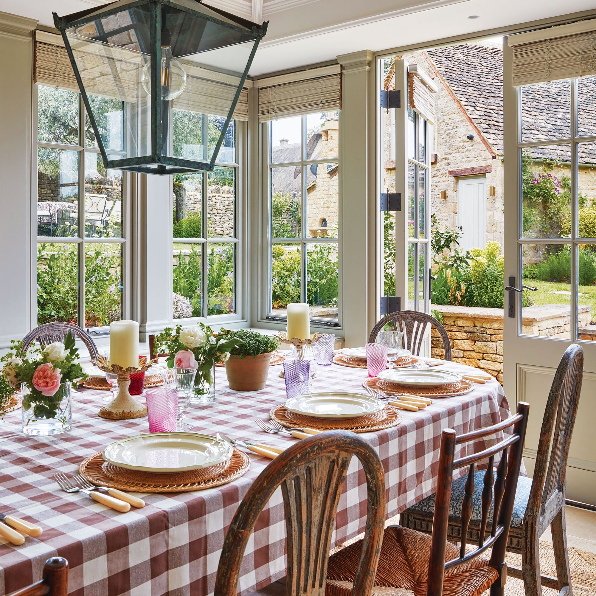 Orangery with lots of light, dining table with wooden chairs and chequered tablecloth