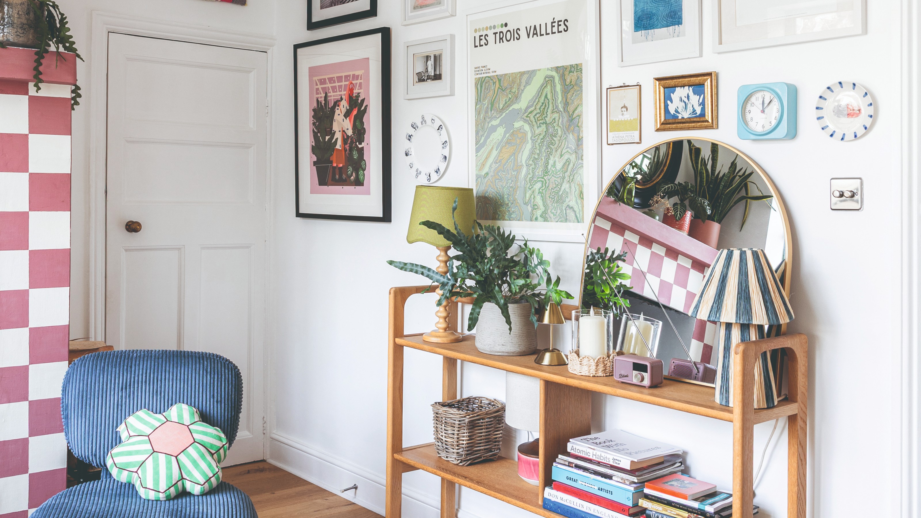 A white-painted living room with a gallery wall, a console table displaying decor and books and a chequerboard-painted fireplace in pink and white