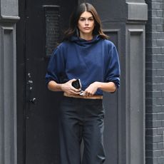 Kaia Gerber wears a navy sweatshirt, black pants, and red, white and blue sneakers.