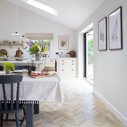 country cottage kitchen with cream coloured shaker cabinets and cup handles, a charcoal coloured dining table with white tablecloth and sliding doors that lead to the garden