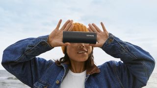 a woman holding up the sonos roam bluetooth speaker