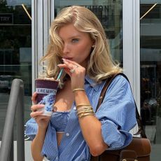 Elsa Hosk wears a brown Gucci bag with a blue and white stripe shirt, blue and white bralette and a stack of gold bracelets.