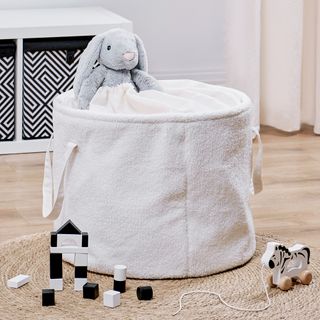 Cream boucle storage bag with plush bunny inside and toys surrounding it