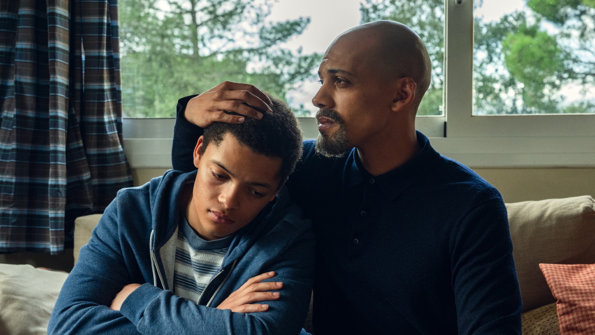 a young man is comforted by his father as they sit in front of a window in their home in the Netflix show &lsquo;The Witness&rsquo;