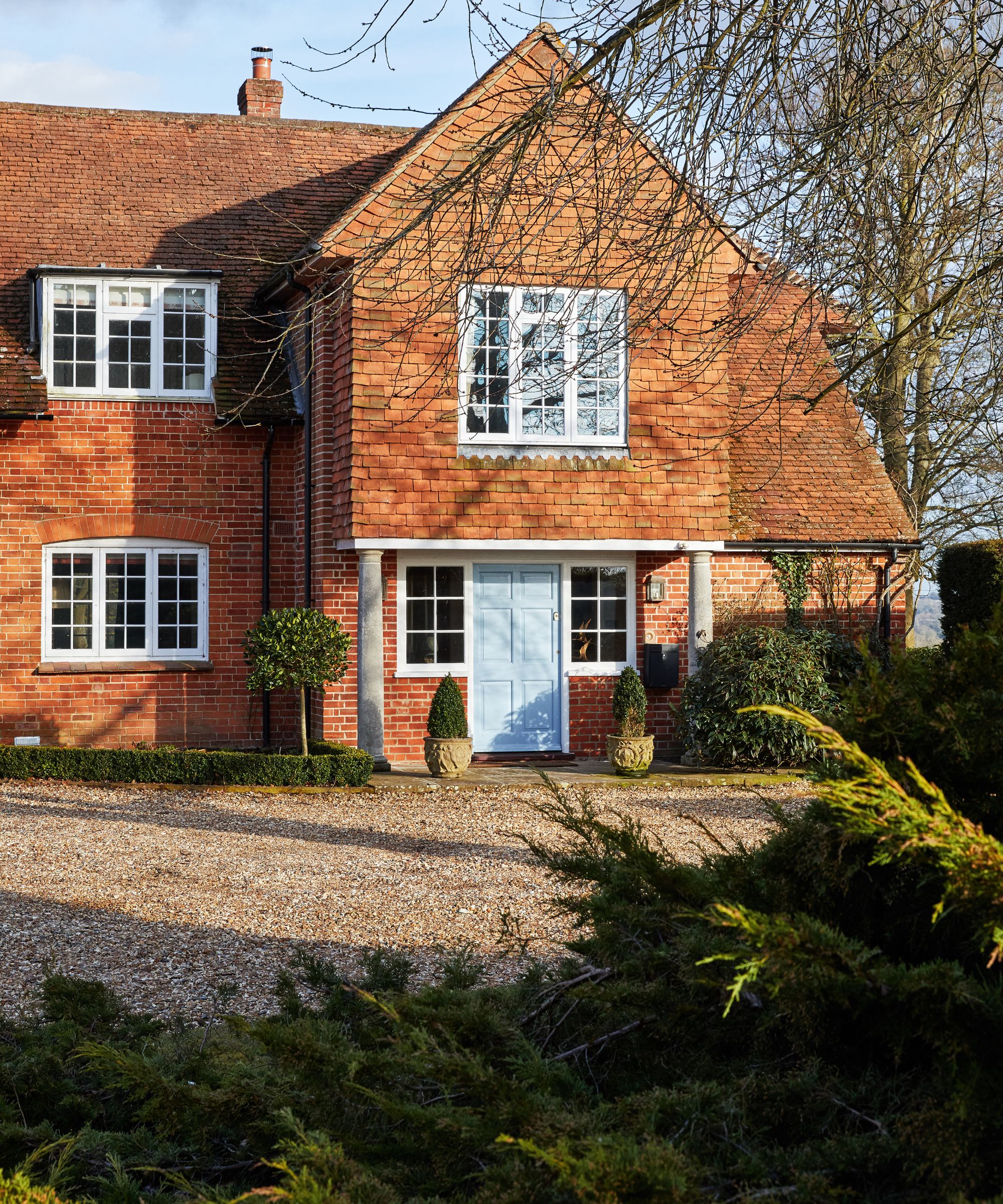A red brick house with a gravel driveway and large bushes in the foreground