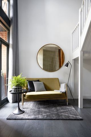 A mustard sofa, styled with circular mirror, cushions and plants