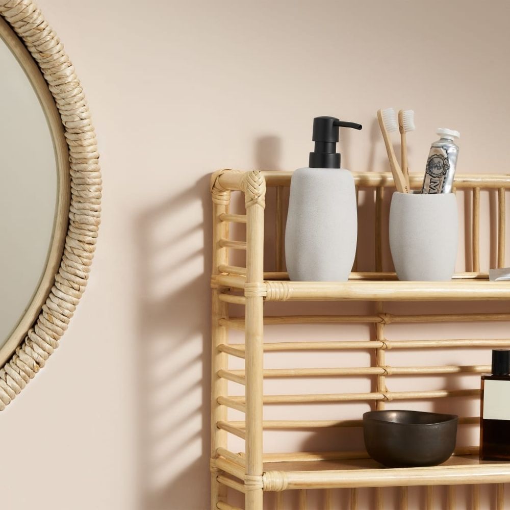 2 wooden toothbrushes and toothpaste in grey holder next to handwash container on a bamboo stand next to mirror
