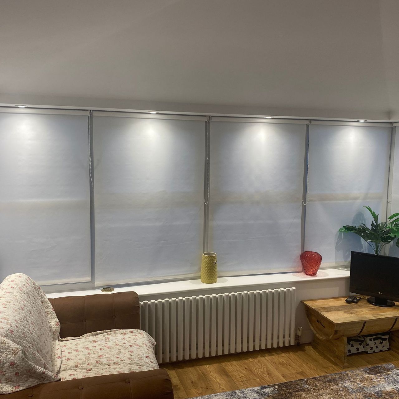 White conservatory blinds with spotlights above, brown leather look chair with throw, radiator and wooden floor