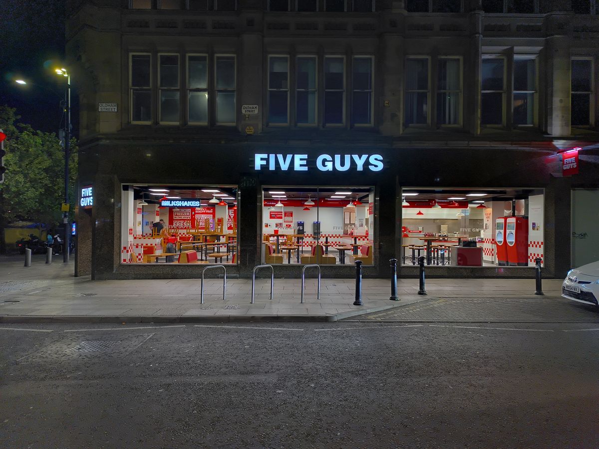 A brightly lit Five Guys restaurant storefront at night