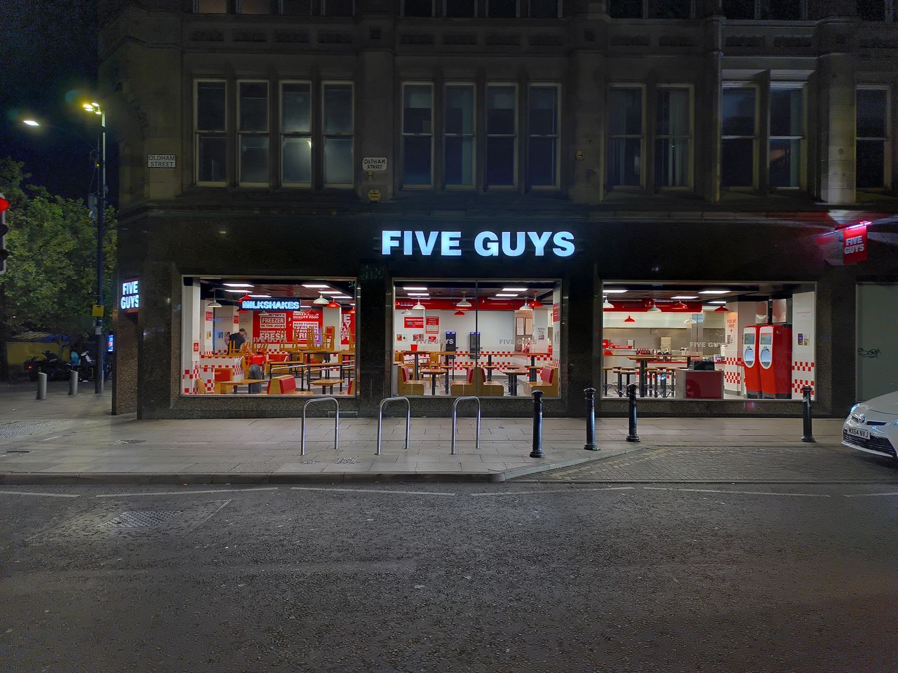 A brightly lit Five Guys restaurant storefront at night