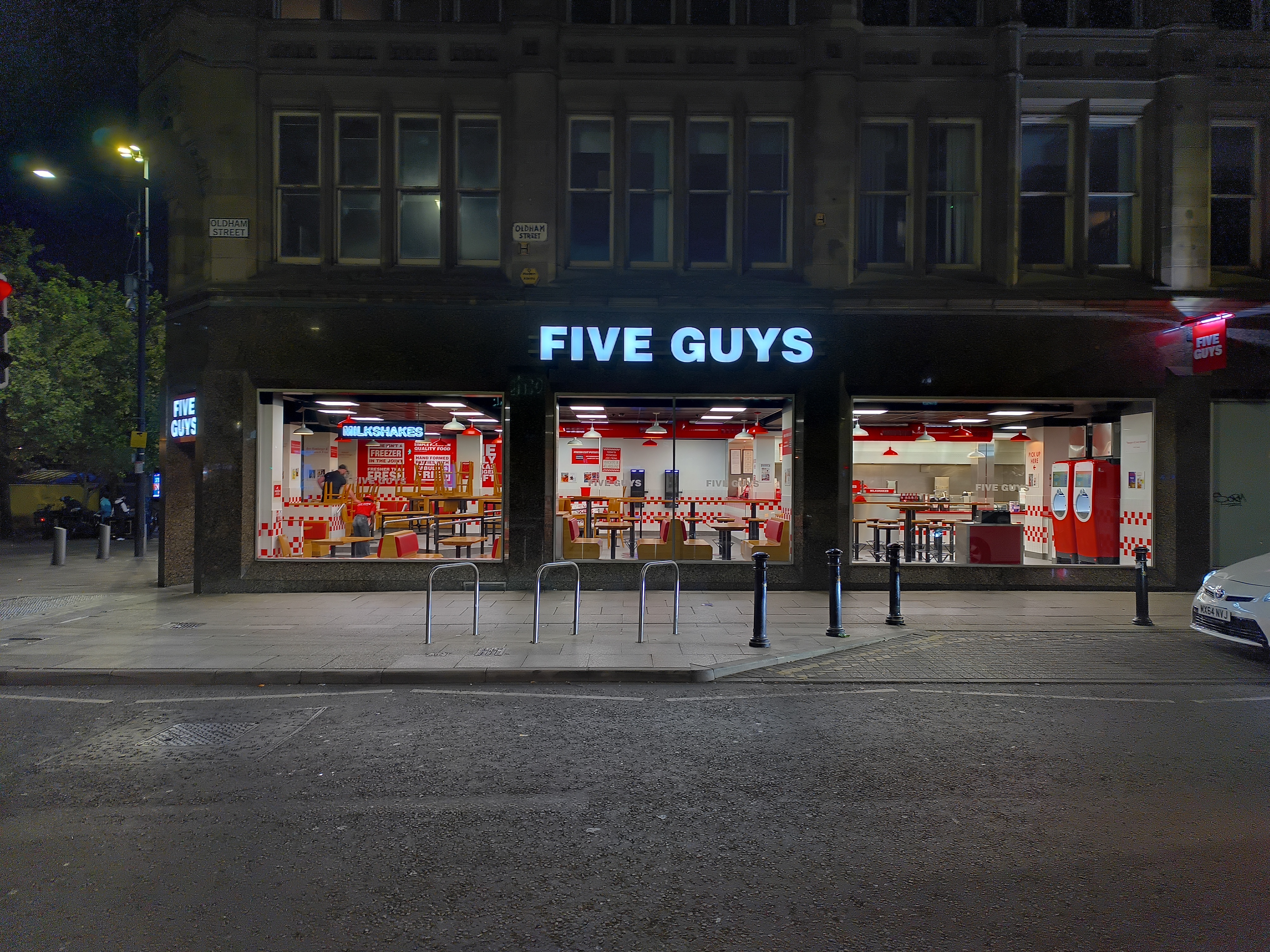 A brightly lit Five Guys restaurant storefront at night