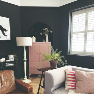 A living room with near-black walls painted in Farrow & Ball's Railings with a pink cabinet in an arched alcove