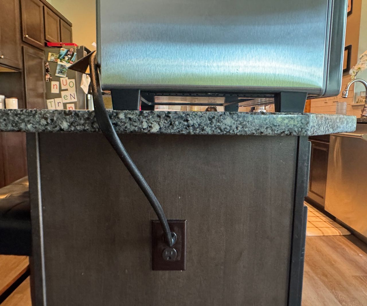The Typhur Sync Air Fryer Oven on a granite work top plugged into an outlet on the side of an island