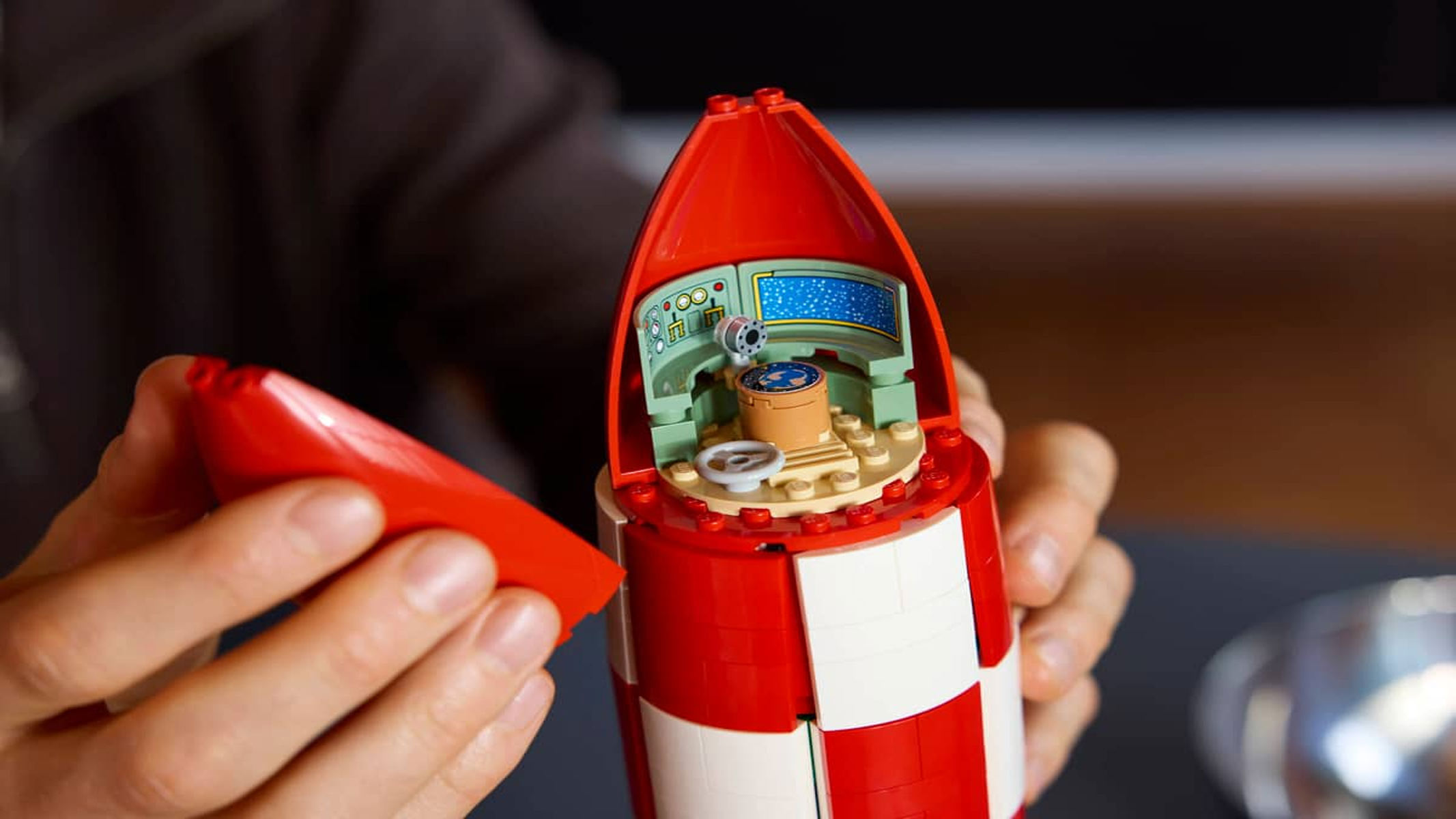 A brick built rocket featuring red and white squares on its exterior is posed alongside six astronaut figures that come with the set.