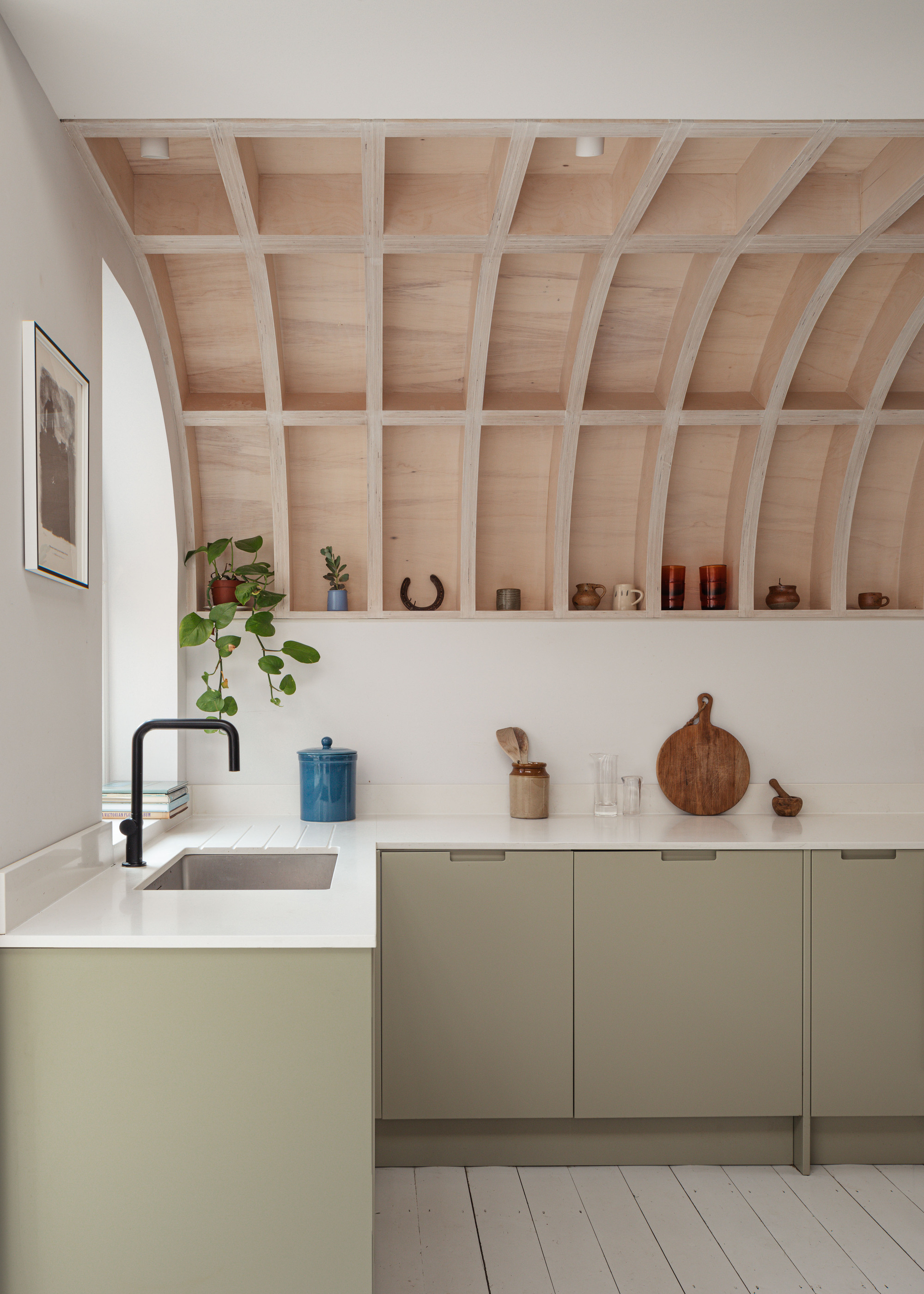 A minimalist kitchen with a wooden vaulted ceiling, green slab cabinets, and a white quartz countertop