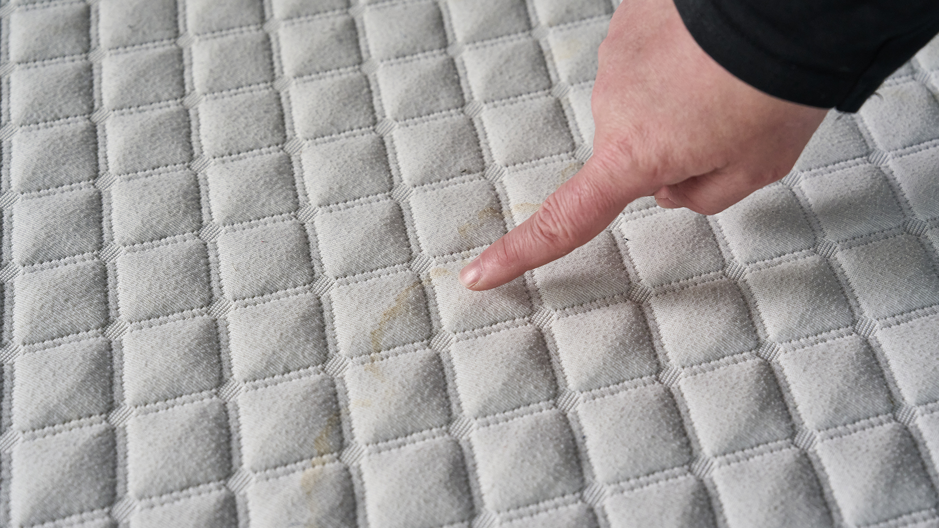 A woman pointing at a urine stain on a mattress