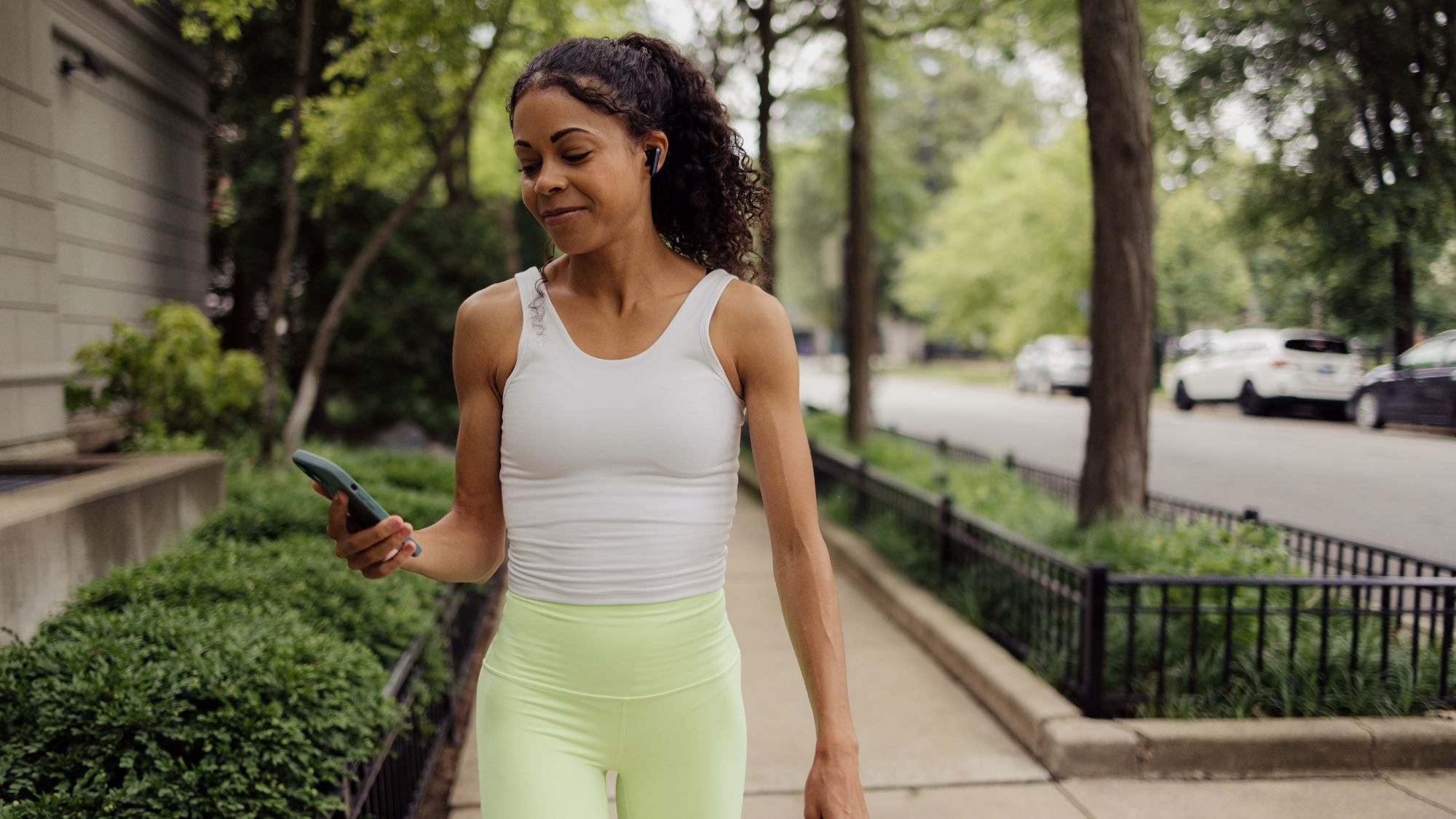 A woman walking on the street in white and green activewear, aiming for 7000 steps a day