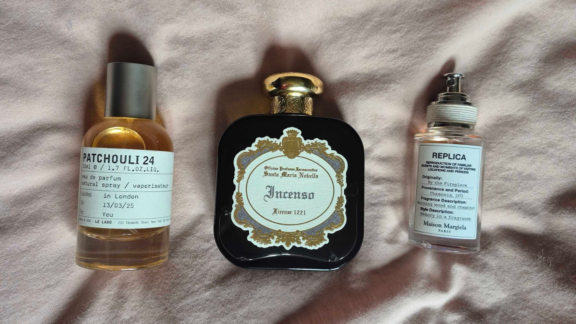 A collection of &#039;fireside&#039; perfumes featured in this guide, including Le Labo&#039;s Patchouli 24, Santa Maria Novella&#039;s Incenso and Maison Margiela&#039;s By The Fireplace perfumes/ pictured on a pink bedding background