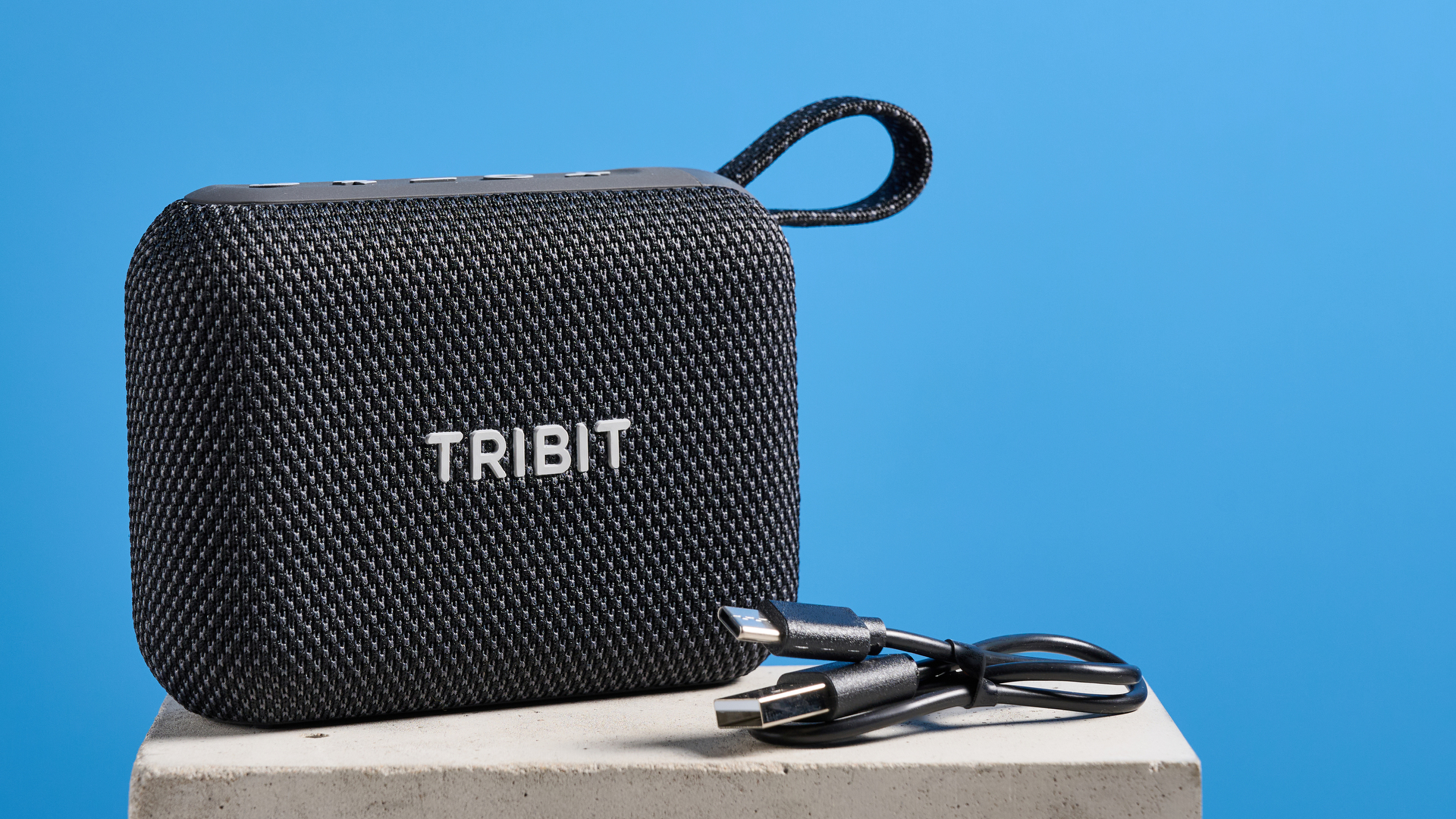 The Tribit PocketGo speaker in black photographed on a blue background.
