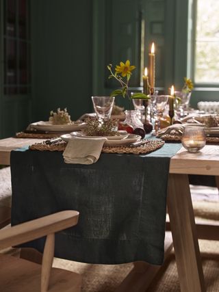 fall table setting with green runner, cream plates, candles, tea lights, green painted walls