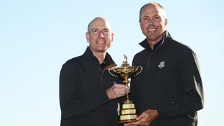 Matt Kuchar and Jim Furyk holding up the Ryder Cup trophy after winning in 2018