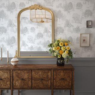 A hallway with the top half of the wall covered in a toile de jouy wallpaper in white and grey