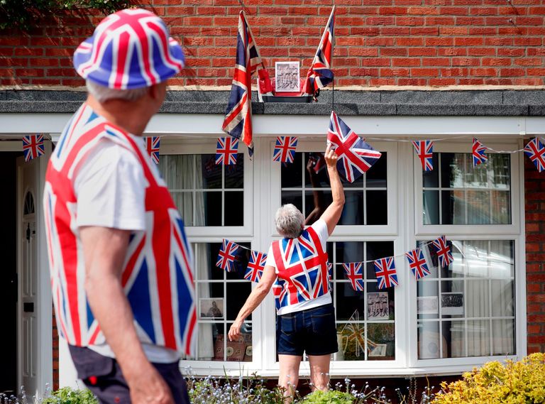 A woman and man decorate their house with Union Jack flags for VE day 2021