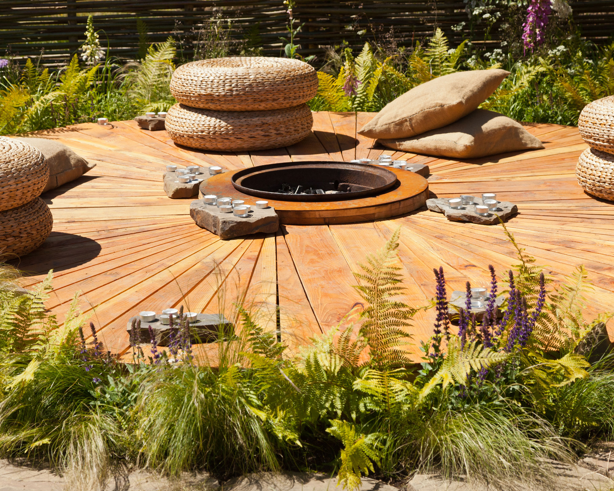 circular wooden deck with cushions and candles, surrounded by naturalistic planting