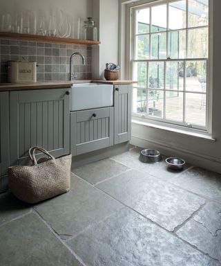 A dark mudroom with two dog bowls, a sink area and a large window