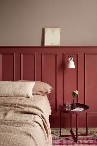 red bedroom with red painted panelling, pink upper wall, pink linen bedding, red bedside, wall light